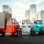 Electric rickshaws in various colors displayed on a city street with modern skyscrapers in the background.