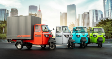 Electric rickshaws in various colors displayed on a city street with modern skyscrapers in the background.