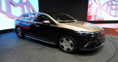 Luxury black SUV on display at an auto show with a stylized logo in the background.