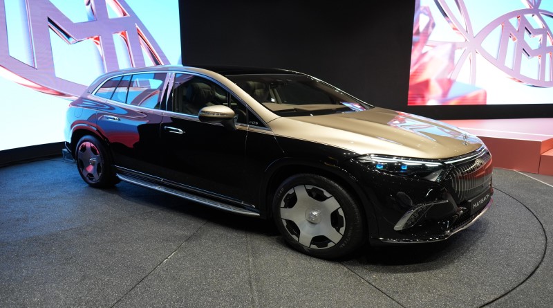 Luxury black SUV on display at an auto show with a stylized logo in the background.